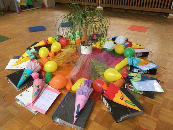 Schultüten und Luftballons liegen im Kreis um einen kleinen Baum, bereit an die Kinder ausgeteilt zu werden, die gesegnet die Kita in Richtung Schule verlassen.